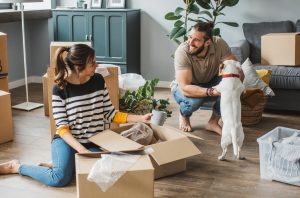 happy couple petting small dog while unpacking moving boxes